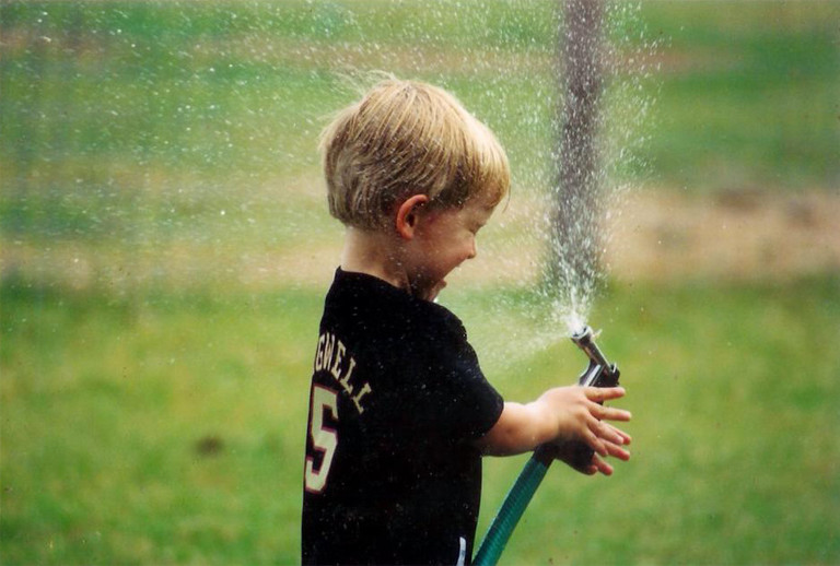 Image of Joshua as a child spraying water from a hose into his face.