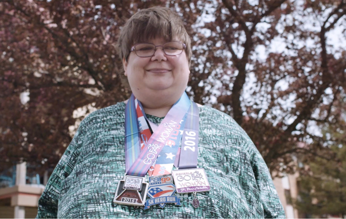 This is a photo of Angie. It shows her wearing three medals on ribbons around her neck – the medals are awards from different events she’s been part of. She’s looking at the camera and smiling.