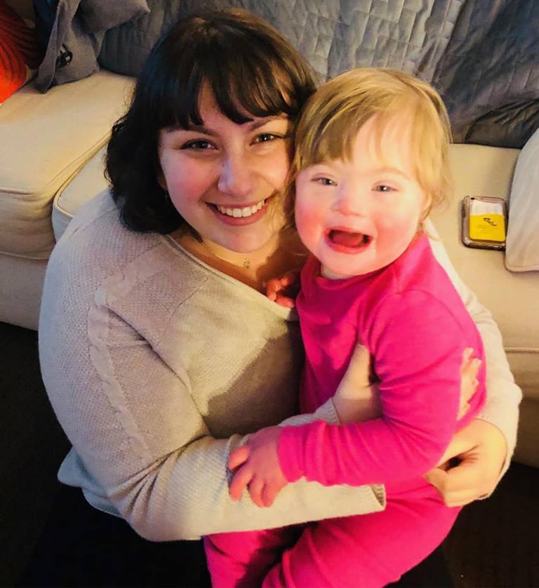 A photo of the article author, Sara Jo Soldovieri, seated and holding a toddler with Down syndrome. Their cheeks are pressed together and they’re looking at the camera and smiling.
