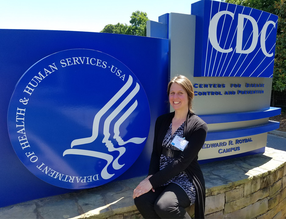 Photo of Jennifer Hall-Lande seated in front of CDC headquarters sign.